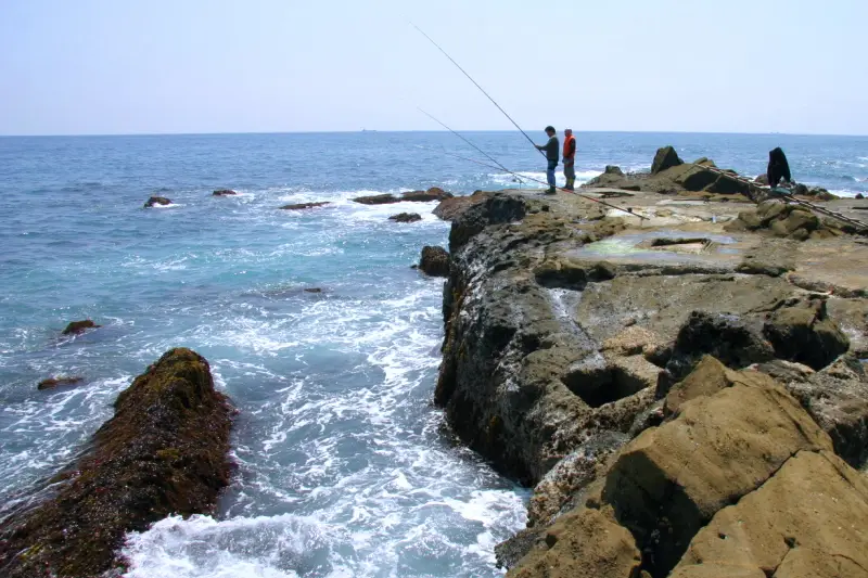 波しぶきを上げる荒々しい岩場で磯釣りを楽しむ釣り人の姿