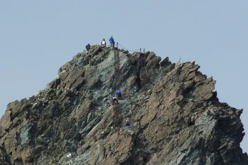 垂直の鉄ハシゴを登る登山者が見える山頂直下の様子