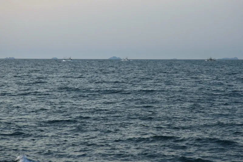 沖合を漁船が通り過ぎ、その先に見える無人島の七ツ島
