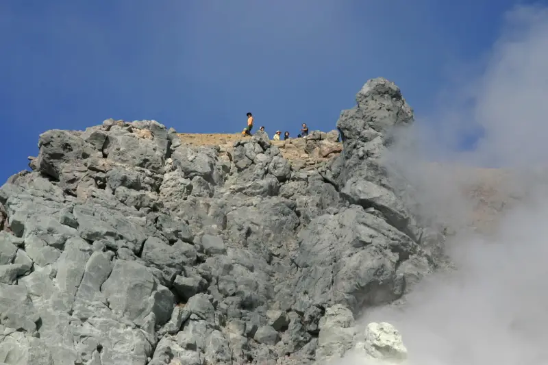 垂直の断崖を見上げると山頂から下を眺める登山者の姿
