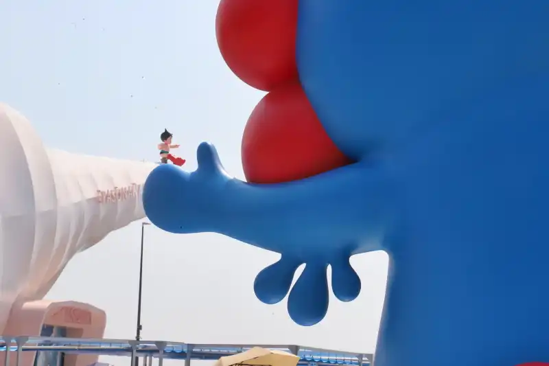 後ろから撮影したミャクミャクの手に座るアトム